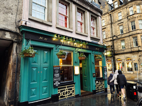 The Albanach pub on the Royal Mile in Edinburgh, Scotland UK, historic green facade with hanging baskets and wet cobblestone street