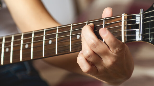 Close-up of girl's hands playing electric guitar indoors