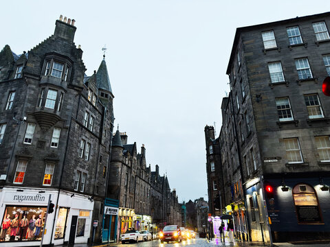 Rainy evening on the Royal Mile in Edinburgh, Scotland UK with historic stone buildings, lit shopfronts and reflective wet cobblestone street