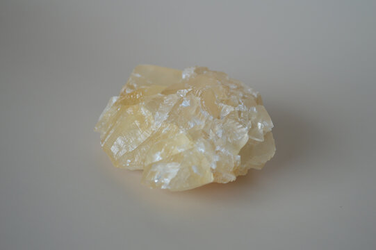 Natural raw yellow calcite crystal mineral specimen with translucent crystalline layers on a neutral grey background for geology and alternative healing concepts.