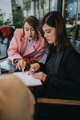 Two professional women collaborate over notes and a tablet during a business meeting. They review documents and discuss plans while seated together in a cafe. © qunica.com