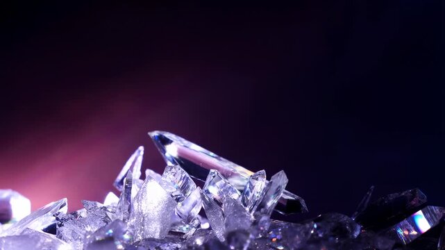 Slow motion close up of crystal shards tumbling and settling on reflective dark surface in studio setting