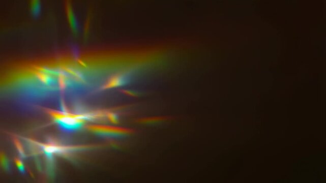 Slow motion pan of lens flare and prism rainbow light shifting across dark studio background with refracted beams and colorful glare