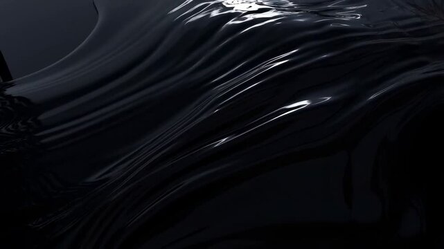 Slow motion close up of glossy black liquid rippling and flowing across surface in dark studio with reflective highlights and soft directional light