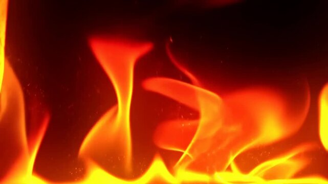 Slow motion closeup of flames rising and flickering on dark studio background, fire tongues dancing and glowing in hearth, intense orange yellow motion