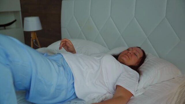 Middle aged woman in pajamas tosses and turns in bed, unable to sleep. She suffers from insomnia, experiencing a restless night with disturbed sleep. Concept of stress, discomfort and sleep problems