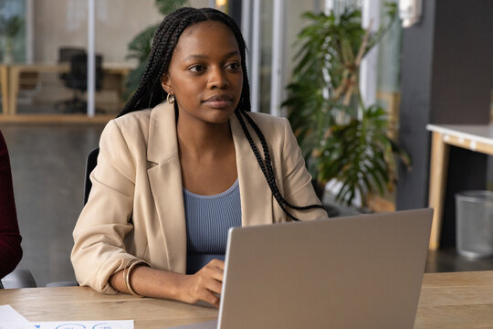 Silver laptop is resting on wooden table in modern office with printed charts nearby