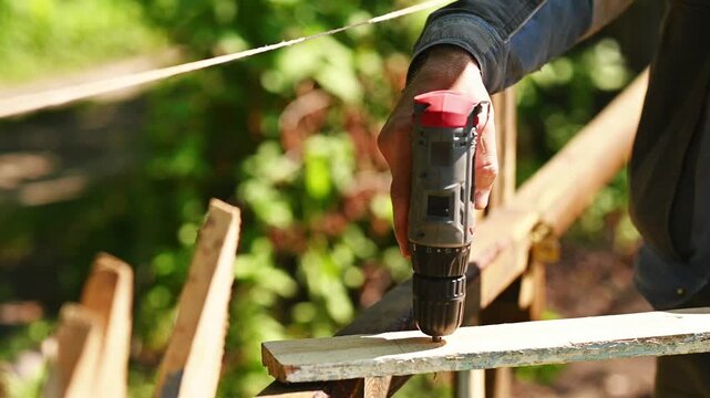 cordless screwdriver machine in hand of a man creating a hole in wood plank. Drill movement captured in detail, outdoor working scene, building and repair concept, manual craftsmanship