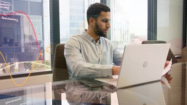 Analyst reading doc and typing on laptop causing finance overlays moving across man and laptop