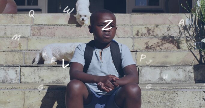 Sitting child squinting on home steps wearing light blue polo black backpack two white dogs nearby