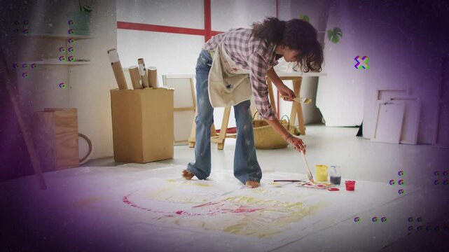 Woman dipping brush into paint cups, creating floor painting in studio, purple dots guiding strokes