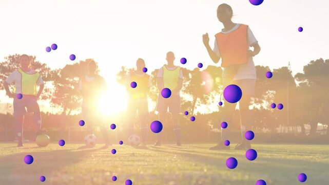 Female player orange bib stepping, dribbling, kicking soccer ball for drill as purple spheres float