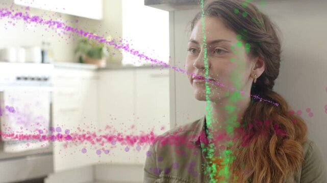 Woman sitting in kitchen by cabinet, particles arcing from left across face and drawing smile, tech