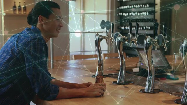 Man lifting, sipping bottle at bar placing it, leaning checking taps while network overlaying