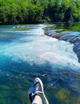 Woman with blue snickers sitting by the green river with waterfalls in magnificent nature