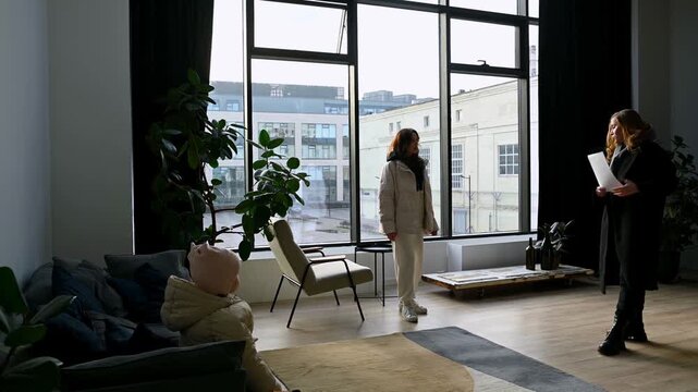 Professional real estate agent guiding a female client through a spacious and modern loft apartment, showing the kitchen and living areas while discussing property details from her clipboard