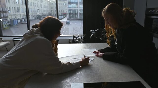 Young woman signing a legal document, rental agreement, or contract with a real estate agent or business advisor in a modern apartment with a city view from the window