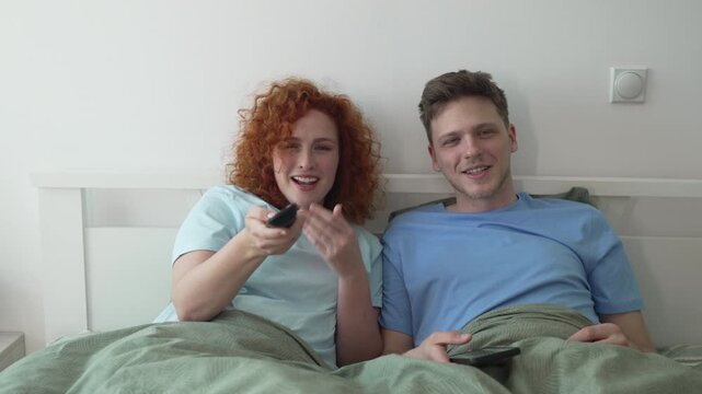 Bored couple watching television and yawning in bed