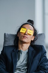 Obraz premium Man with sticky note eyes dozing in chair in neutral studio setting