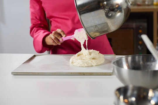 Chef pouring batter from metal bowl onto baking sheet with pink spatula