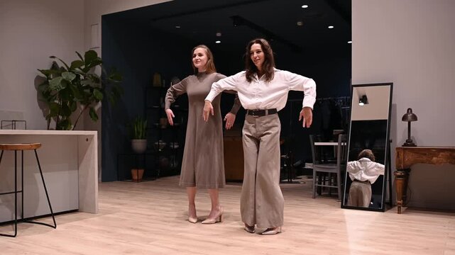 Two young women smiling and dancing in sync in a stylish modern room, showing joyful friendship, energy and coordinated movement during a cheerful rehearsal