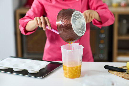 Chef pouring cooked yellow mixture from copper pan into measuring jug