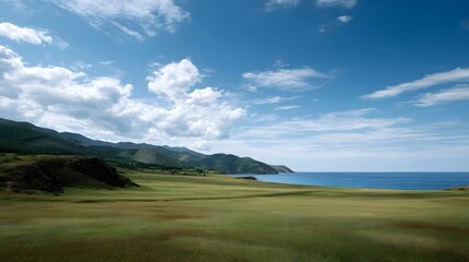 Fototapeta premium A panoramic view of a vast meadow leading toward a calm blue ocean under a dramatic cloudy sky