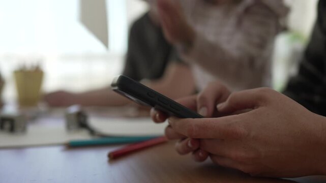 Mother using smart phone while family plays and draws