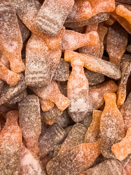 Close-up of sugar coated cola bottle gummy candies creating a textured sweet snack background with brown and orange tones.
