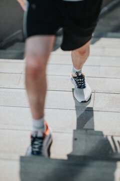 A runner jogs up concrete stairs wearing athletic shoes and shorts. The athlete climbs steps during an outdoor fitness workout, showing movement and effort.