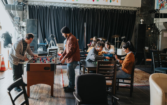 Students play foosball and tabletop games in a casual campus lounge. A group of friends relax and socialize while playing foosball and board games.