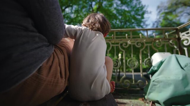Toddler climbing onto chair beside parent on balcony, seeking closeness and comfort, gentle interaction showing attachment and everyday bonding in calm outdoor home setting