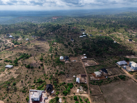 Aerial view of scattered modern homes and developing plots amidst dry, earthy tones and sparse green foliage under a dramatic sky, Elu, Abia, Nigeria.