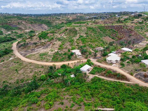 Aerial view of winding dirt roads cutting through sparse vegetation and scattered buildings on hilly terrain, Asaga, Abia, Nigeria.