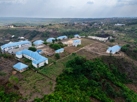 Aerial view of buildings with blue roofs nestled amidst rolling hills and lush greenery, a blend of structures and nature, Ohafia, Abia, Nigeria.