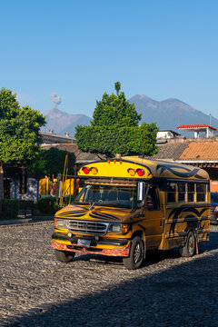 Traditional chicken bus with eruption of the Fuego volcano, Antigua, Guatemala.