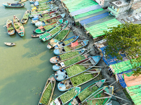 Aerial view of boats laden with produce crowd the riverbank, contrasting with the colorful market stalls, Barishal, Barisal Division, Bangladesh.
