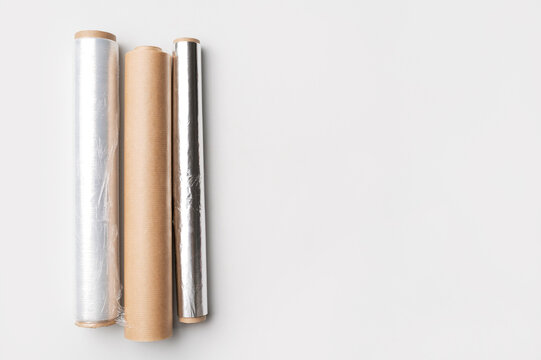 Cling film, aluminum foil, parchment paper on gray background flat lay top view. Kitchen rolls for packaging and storing food