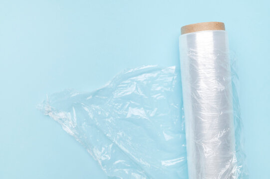 Roll of transparent food wrap for packaging and storing food products on blue background. Kitchen packaging materials, flat lay top view