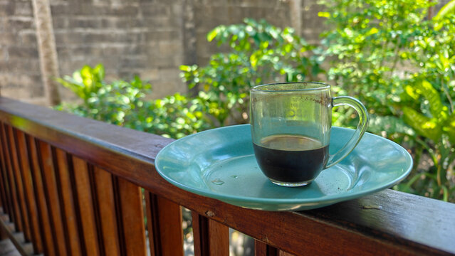 Traditional Black Balinese Coffee in Glass Cup on Wooden Terrace Railing