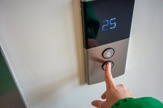hand pressing elevator button in office building corridor, modern control panel with display. Concept: everyday technology use