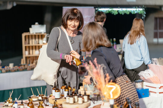 Mature woman testing handmade cosmetic product at local craft market stall