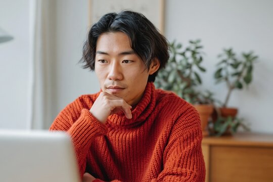 Young asian man studying at home desk with plants near laptop