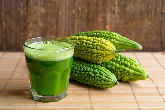 Glass of green bitter gourd juice next to fresh bitter gourds image