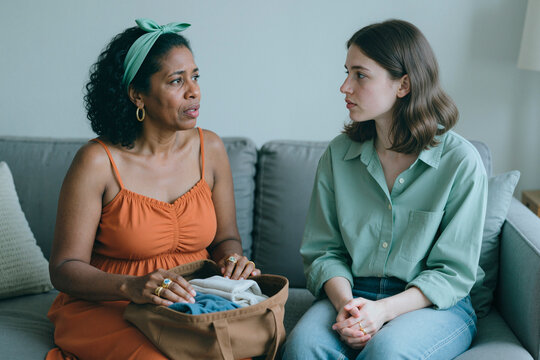 Middle aged Black woman showing packed hospital bag to young adult Caucasian woman, discussing childbirth planning and family support. Useful for maternity care, parenting guidance, counseling