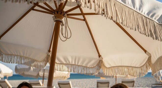 Close up of a white fringed beach umbrella providing shade on a sunny day.
