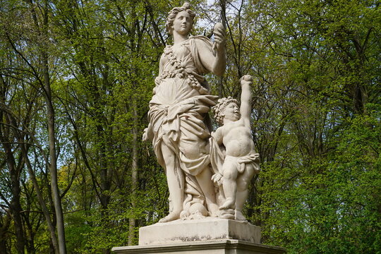 A marble statue of the Roman goddess Flora with a putto stands in the historic rose garden of Tiergarten park, Berlin, Germany.