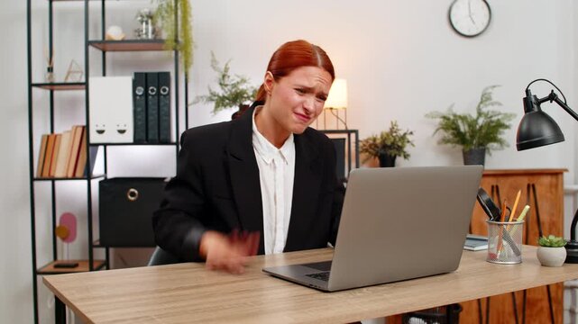 Young businesswoman at home office sees laptop screen freeze slaps table grabs head stressed. Freelancer girl at table hits ctrl alt del waits anxious hoping system recovers soon to keep working again