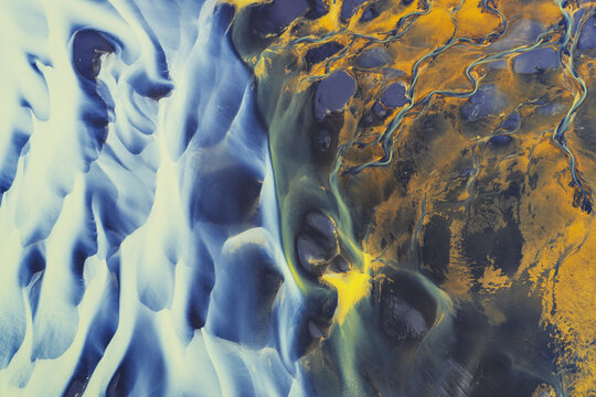 Aerial view of a glacial river delta featuring intricate braided patterns of blue water and bright orange sediment in Iceland.