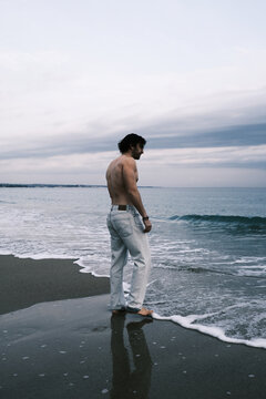 Man standing on a beach with waves gently lapping at his feet